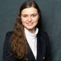 LinkedIn-Profilfoto von Sarah Mayrhofer — dunkler Blazer vor grünem Hintergrund